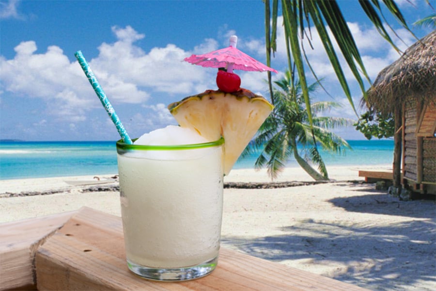 Jamaican Me Crazy Cocktail in a clear glass garnished with pineapple, cherry, umbrella and straw with an ocean background