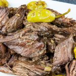 Crock Pot Mississippi pot roast on a white platter garnished with pepperoncini.