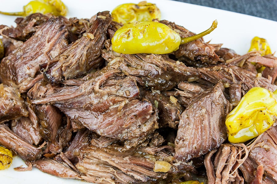 Crock Pot Mississippi pot roast on a white platter garnished with pepperoncini.