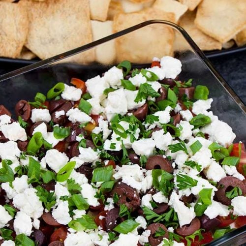 Easy Mediterranean dip in a glass baking dish with pita chips in the background.
