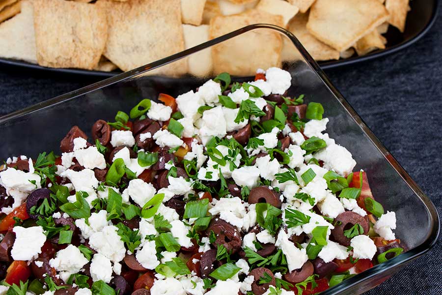 Easy Mediterranean layer dip in a glass baking dish with pita chips in the background.