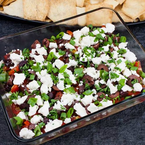 Easy Mediterranean Dip - Layered with hummus, sour cream, tomato, cucumber, roasted red pepper, feta cheese, Kalamata olives and green onions. Perfect for any party or gathering!