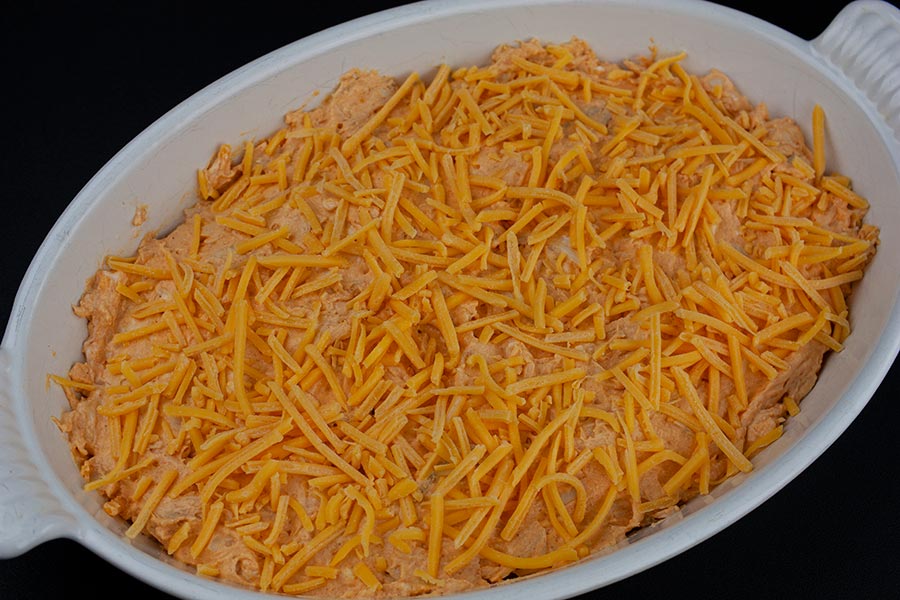 Buffalo Chicken Dip - unbaked dip in a white casserole dish topped with cheddar cheese