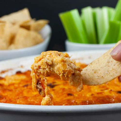 Buffalo chicken dip lifted out of the baking dish with a tortilla chip.