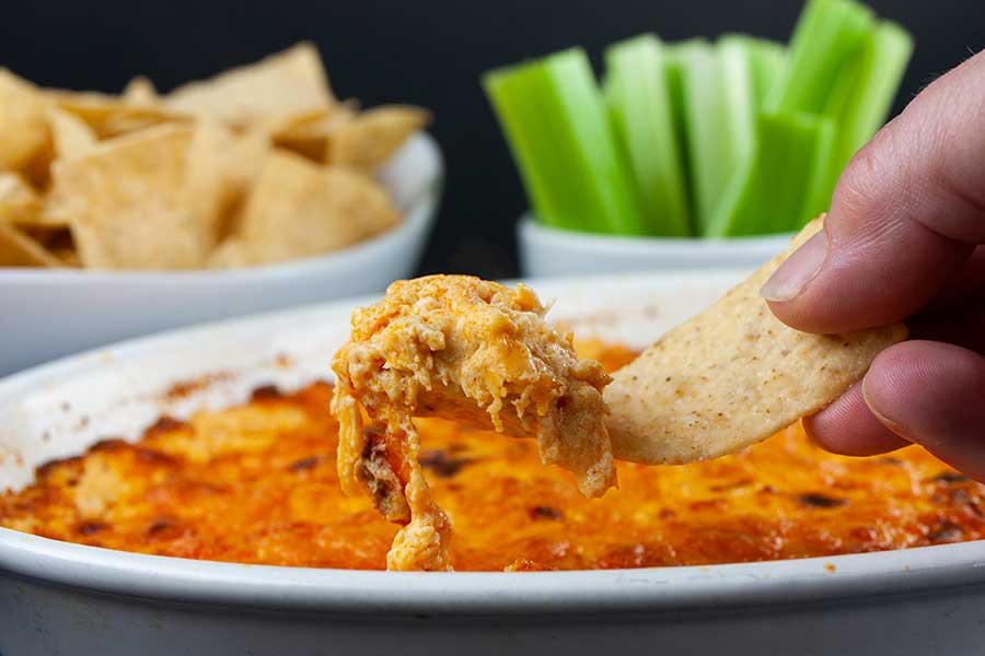 Buffalo chicken dip lifted out of the baking dish with a tortilla chip.