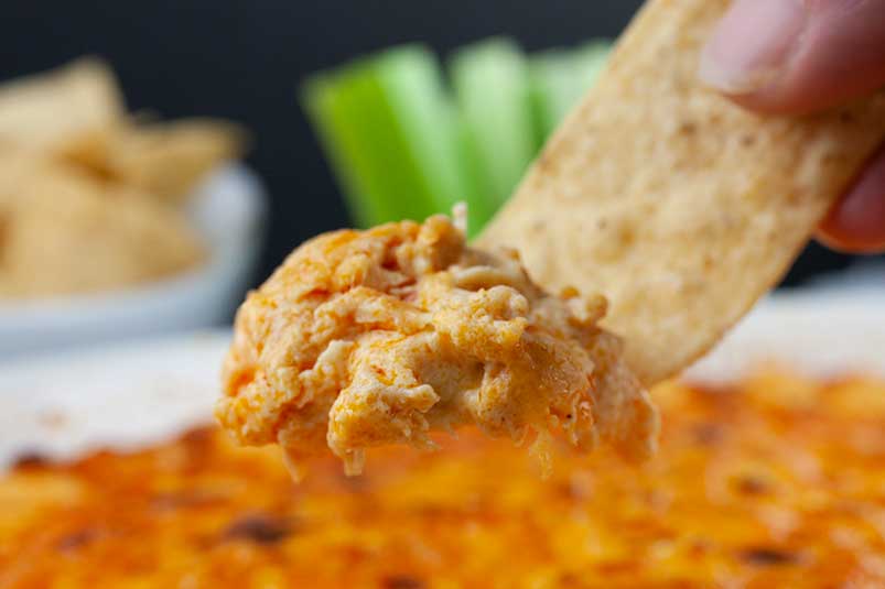 A tortilla strip digging into some buffalo chicken dip.