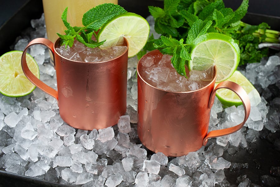 Skinny Moscow Mule - two copper mugs filled with cocktail on a tray of ice garnished with a lime slice and fresh mint leaves
