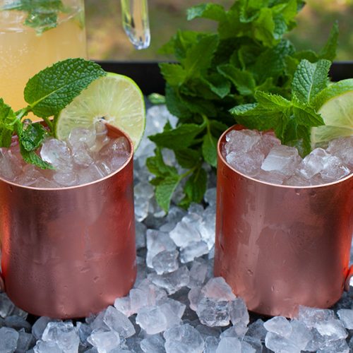 Skinny Moscow mules in copper mugs on a tray of ice garnished with fresh mint.