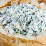 Easy spinach dip in a bread bowl surrounded by bread cubes.