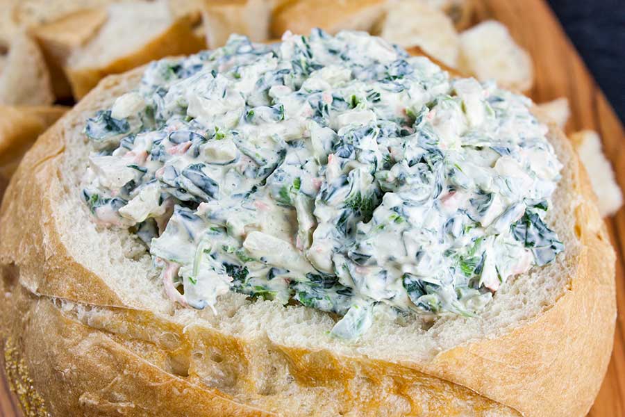 Easy spinach dip in a bread bowl surrounded by bread cubes.