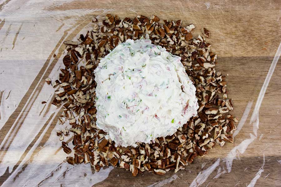 Cheese ball formed and placed on chopped pecans on plastic wrap.