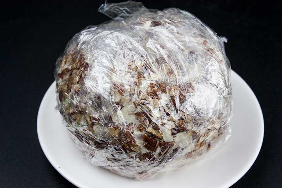 Cheese ball formed and rolled in pecans wrapped tightly with plastic wrap.