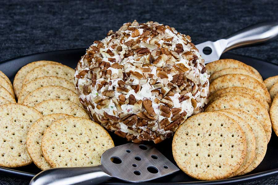 Best pecan crusted cheese ball on black platter surrounded by wheat crackers.