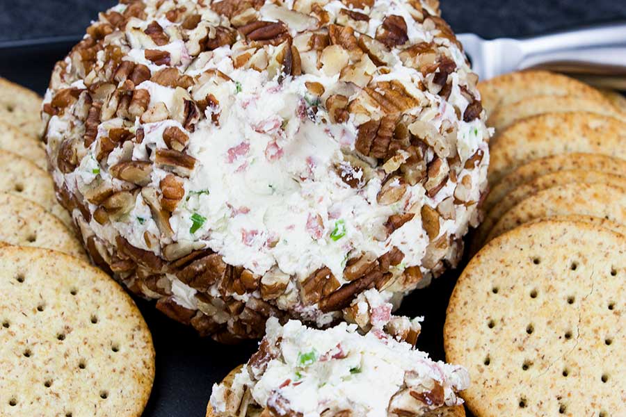 Closeup of the pecan crusted cheese ball on black platter surrounded by wheat crackers.