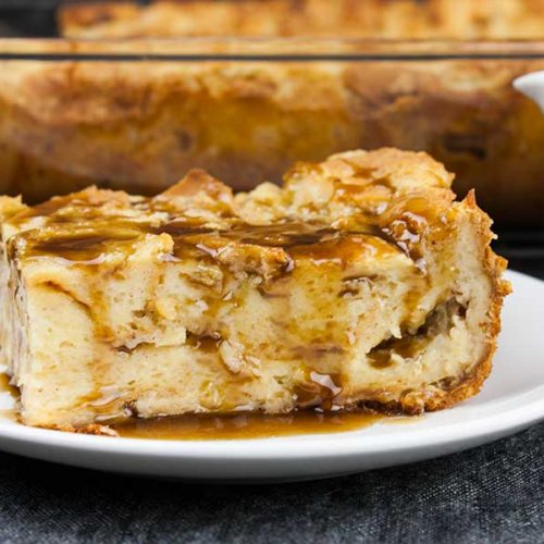 A slice of bread pudding on a white plate drizzled with bourbon sauce.