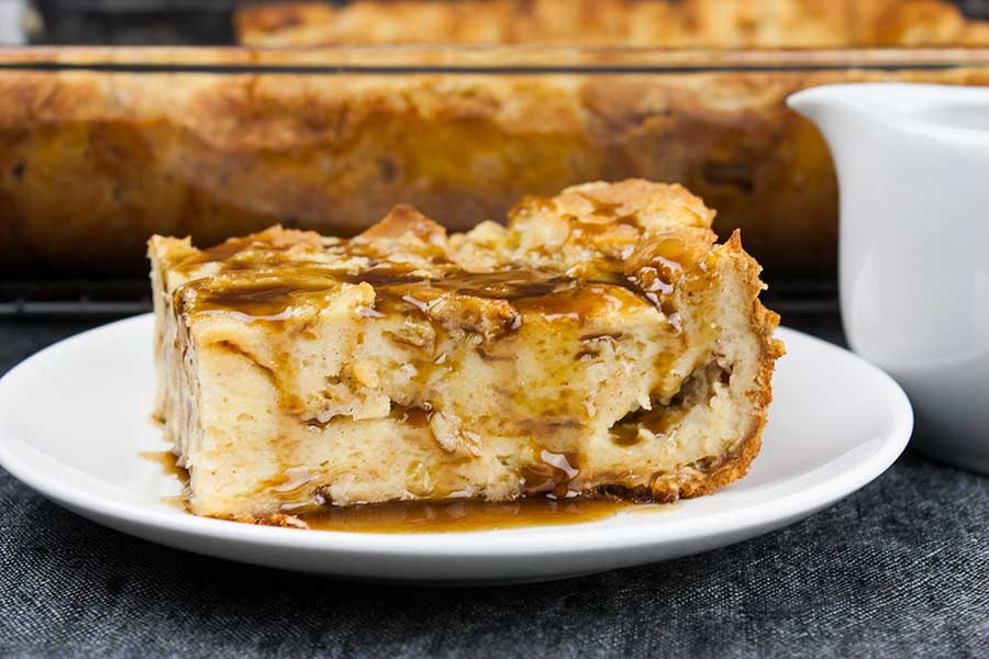 A slice of bread pudding on a white plate drizzled with bourbon sauce.