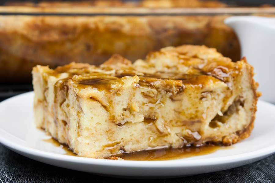 Slice of bread pudding with bourbon sauce poured over the top on a white plate.