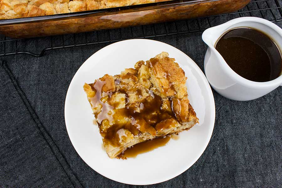 Slice of bread pudding drizzled in bourbon sauce on a white plate.