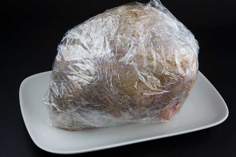 turkey breast wrapped in plastic on a white platter