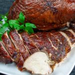 Smoked turkey breast on a white platter garnished with parsley.