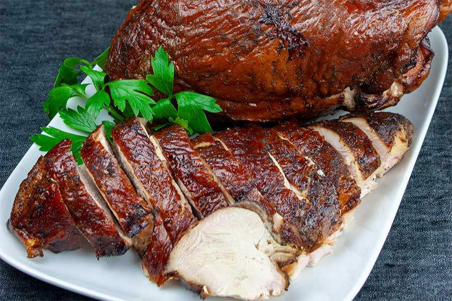 Smoked turkey breast on a white platter garnished with parsley.