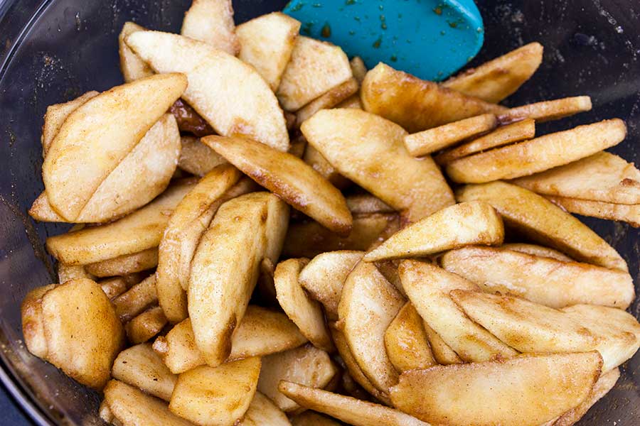 Thinly sliced apples in a glass bowl mixed with sugars and spices.