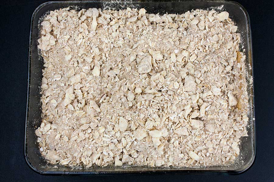 Apples and topping in a glass baking dish.