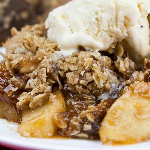 Classic apple crisp with oat topping on a white plate topped with vanilla ice cream.