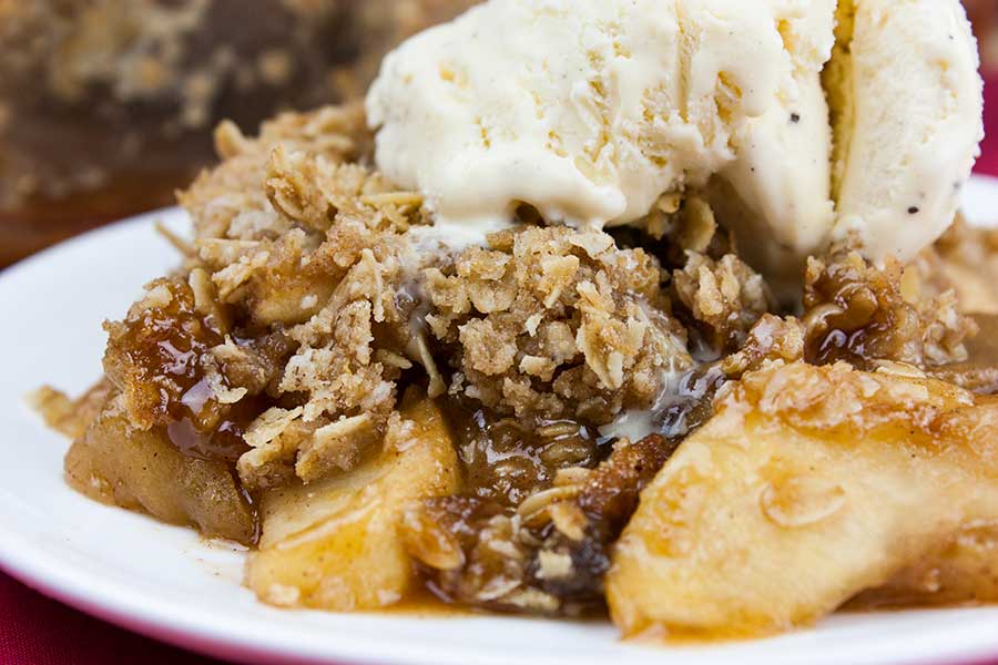 Classic apple crisp with oat topping on a white plate topped with vanilla ice cream.