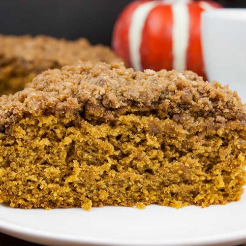 A slice of pumpkin coffee cake with streusel topping on a white plate.