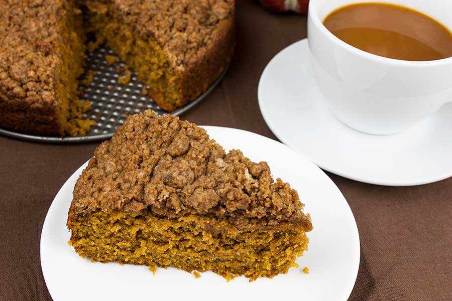 Slice of pumpkin coffee cake on a white plate with a cup of coffee in a white cup.