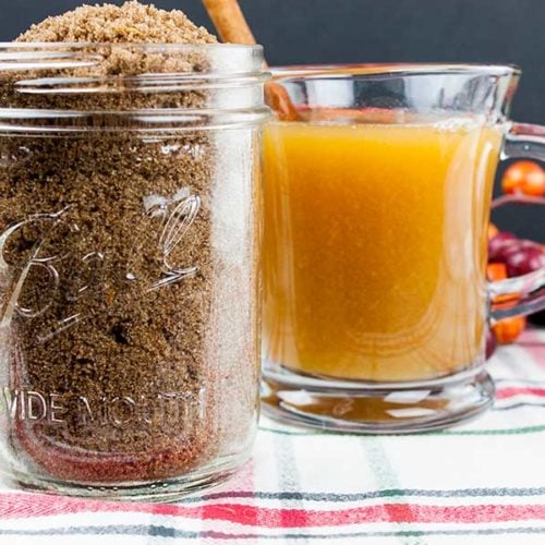 Apple cider spice mix in a mason jar with a glass mug of apple cider next to it.