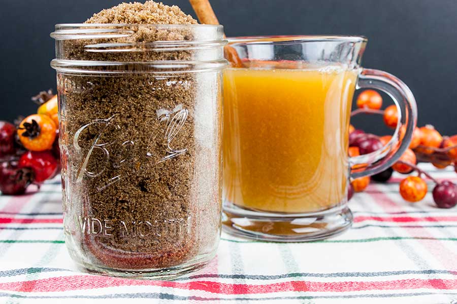 Apple cider spice mix in a mason jar with a glass mug of apple cider next to it.