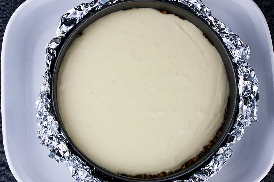 Unbaked eggnog cheesecake batter in springform pan placed in water bath.