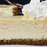 A slice of eggnog cheesecake with gingersnap crust on a white plate garnished with whipped cream.