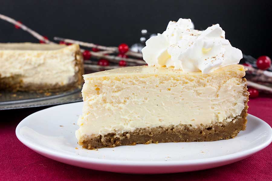 A slice of eggnog cheesecake garnished with whipped cream on a white plate.