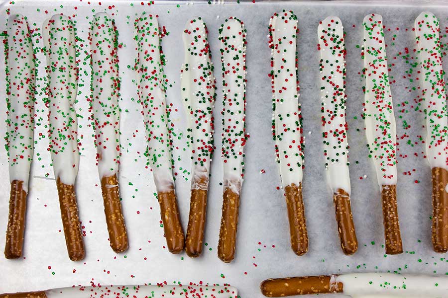 Chocolate Covered Pretzel Rods - pretzel rods dipped in white chocolate with green and red sprinkles placed on parchment paper