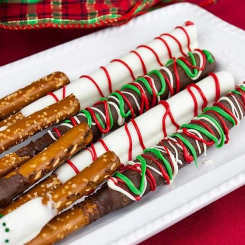 Chocolate covered pretzel rods on a white plate with a red placemat underneath.
