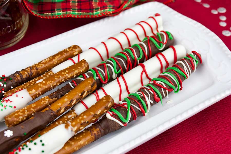 Chocolate covered pretzel rods on a white plate with a red placemat underneath.