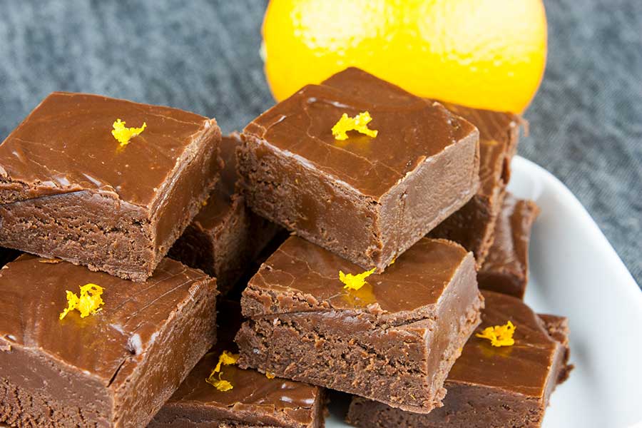 Chocolate orange fudge pieces garnished with orange zest stacked on a white plate and .