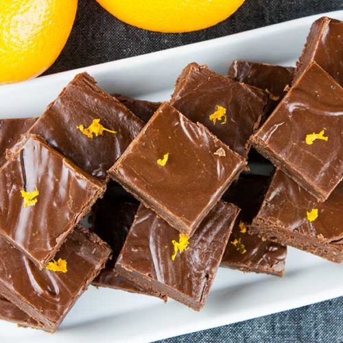 Chocolate orange fudge on a white rectangle platter garnished with orange zest.