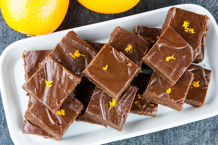 Chocolate orange fudge on a white rectangle platter garnished with orange zest.