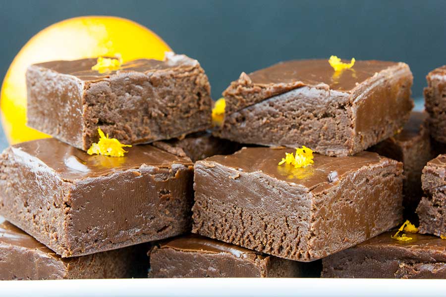 Closeup of fudge cut in squares placed on a white plate and garnished with orange zest.