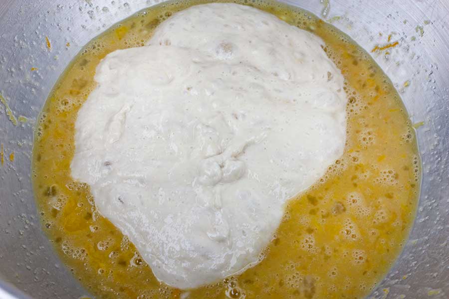 Panettone starter added to the egg mixture in a metal mixing bowl.