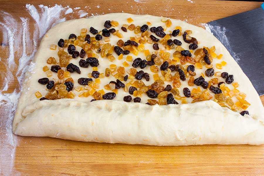 The panettone dough rolled out with the fruit sprinkled over and starting the rolling process.