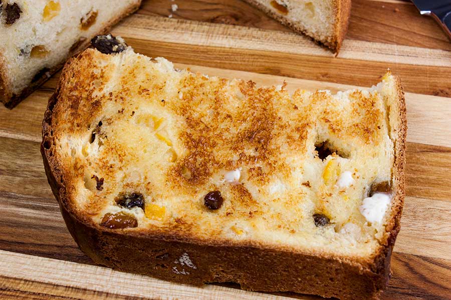 Toasted and buttered slice of panettone bread on a wooden board.