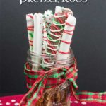 Chocolate covered pretzel rods in a mason jar wrapped with a Christmas ribbon.