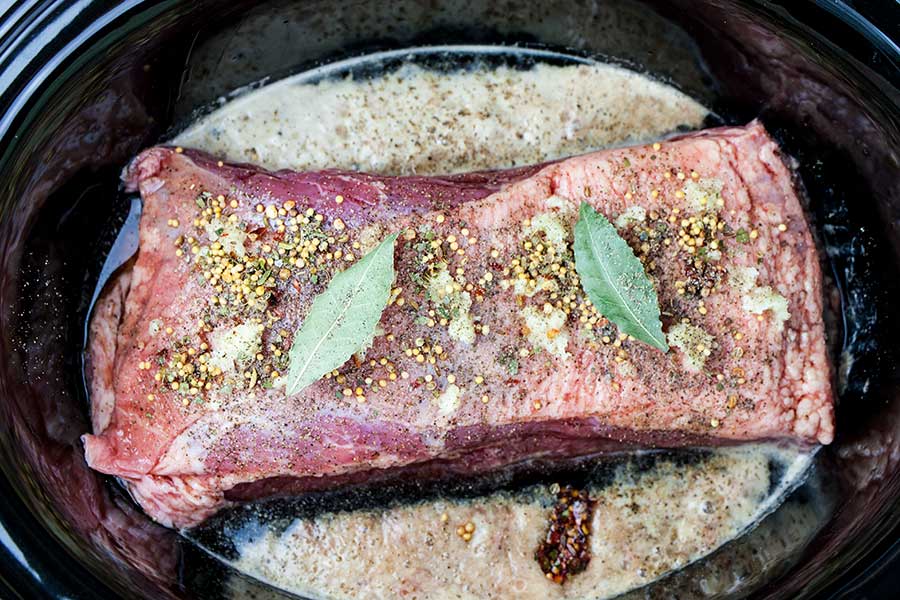 Raw corned beef, spices, and liquids in the crock of the slow cooker.