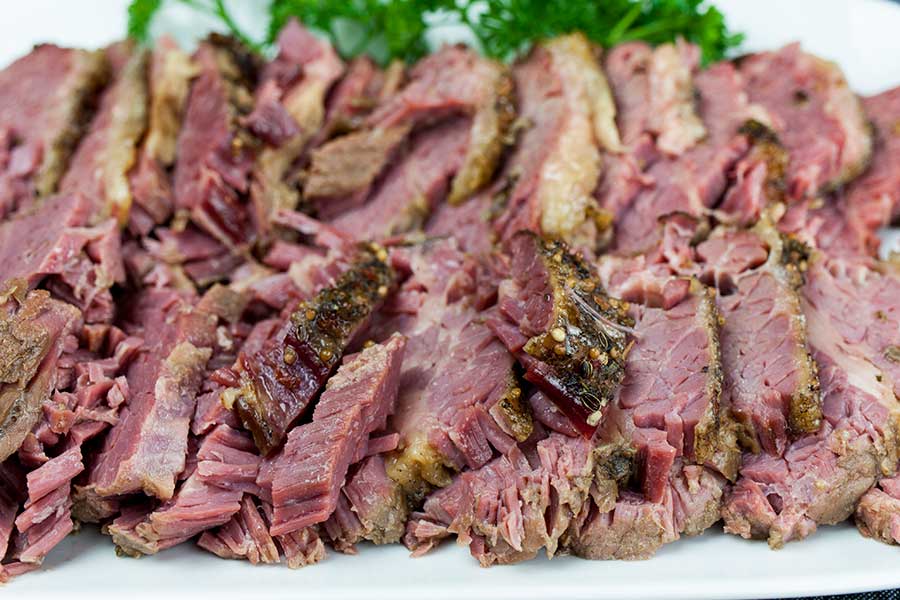 Slow cooker corned beef on a white plate garnished with parsley.