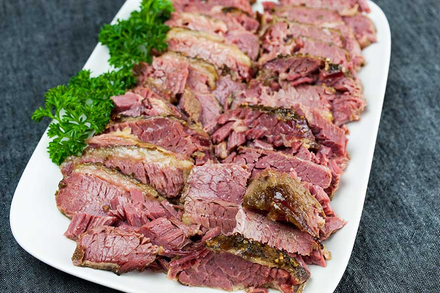 Slow cooker corned beef sliced on a platter garnished with parsley.